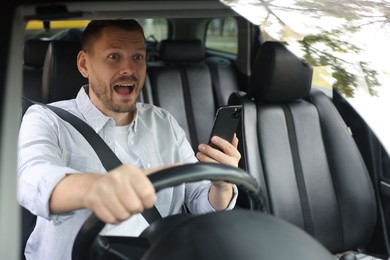 Photo of Emotional man with smartphone driving modern car, view through windshield