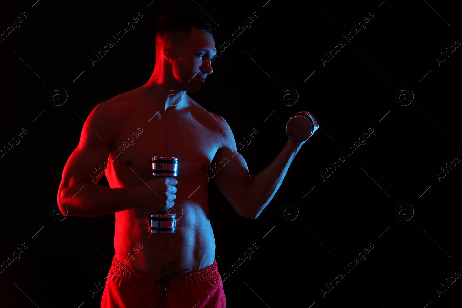 Photo of Man exercising with dumbbells in red light on black background