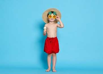 Photo of Cute little boy in beachwear with ice cream on light blue background