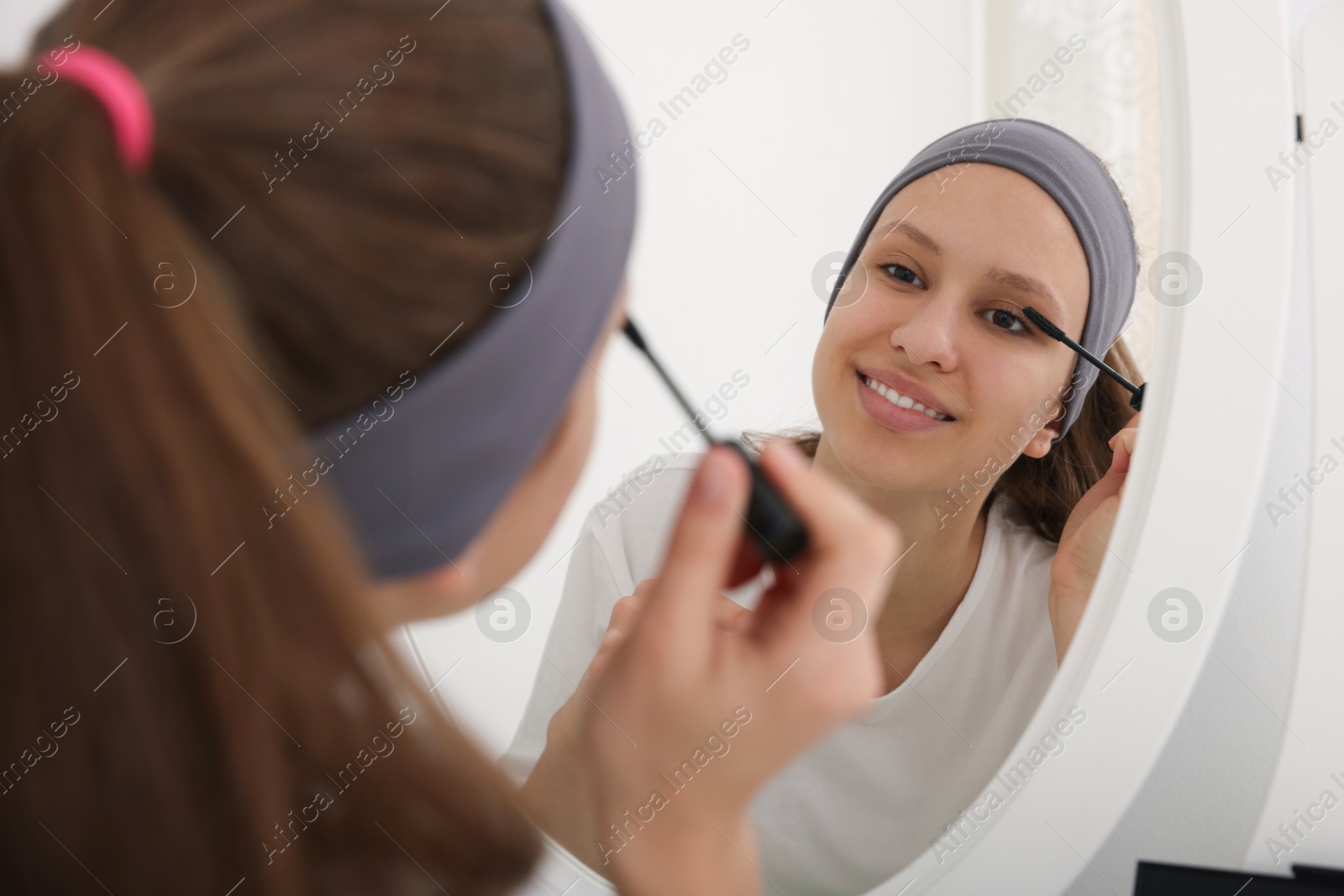 Photo of Teenage girl applying mascara near mirror indoors