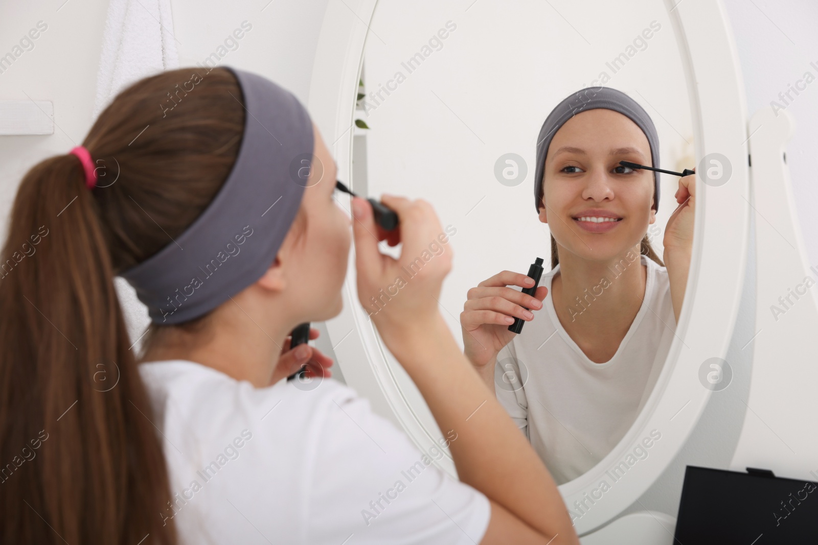 Photo of Teenage girl applying mascara near mirror indoors