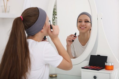 Photo of Teenage girl applying mascara near mirror indoors