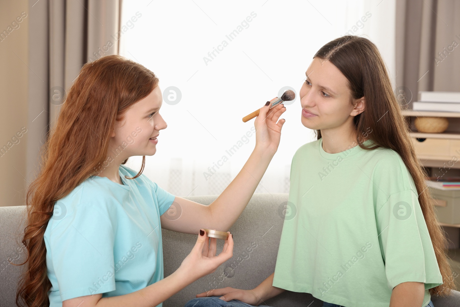 Photo of Teenage girl applying blush on her friend's face indoors