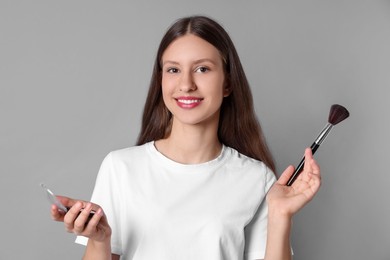 Photo of Smiling teenage girl with blusher and makeup brush on grey background