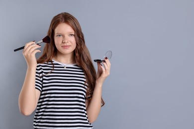 Photo of Teenage girl applying blusher with makeup brush on grey background. Space for text