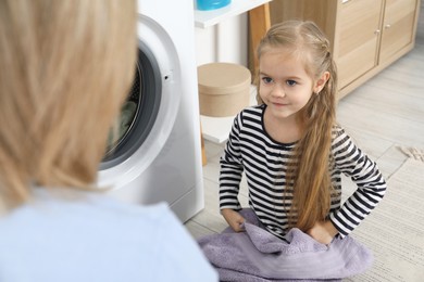 Photo of Little girl helping her mom doing laundry at home