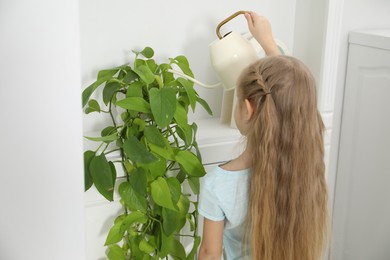 Photo of Little helper. Cute girl with watering houseplant at home