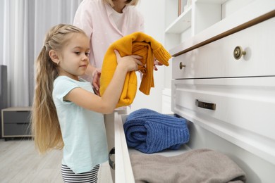 Little girl helping her mother putting clothes into drawers at home