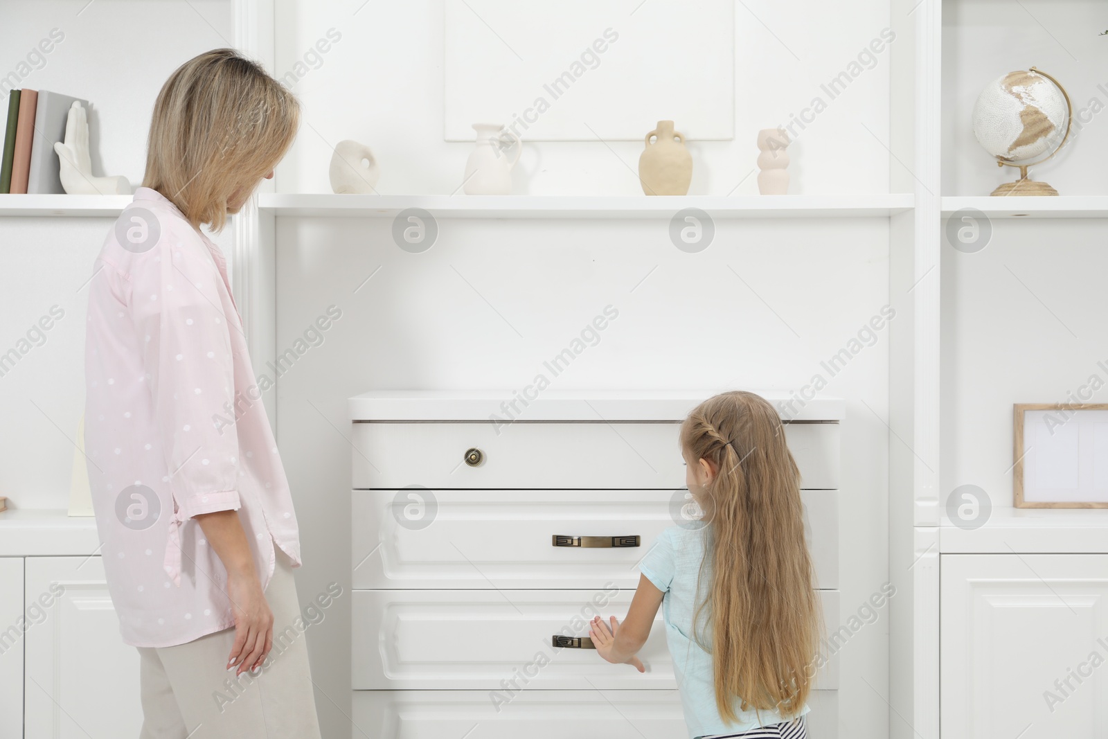 Photo of Little girl helping her mother putting clothes into drawers at home