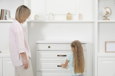 Little girl helping her mother putting clothes into drawers at home