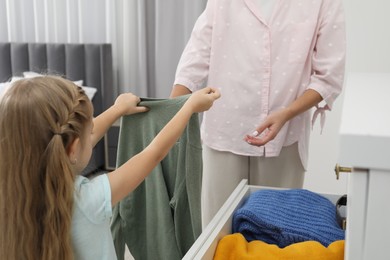 Photo of Little girl helping her mother putting clothes into drawers at home