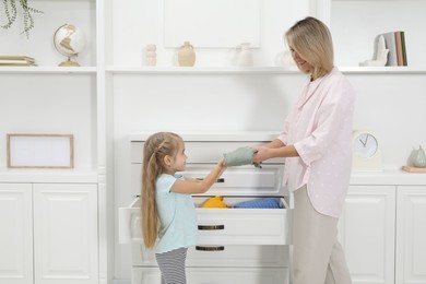 Photo of Little girl helping her mother putting clothes into drawers at home