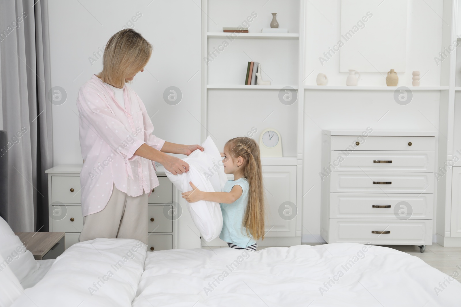 Photo of Little girl helping her mother making bed at home