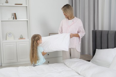 Little girl helping her mother making bed at home