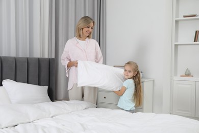 Photo of Little girl helping her mother making bed at home