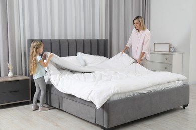 Photo of Little girl helping her mother making bed at home