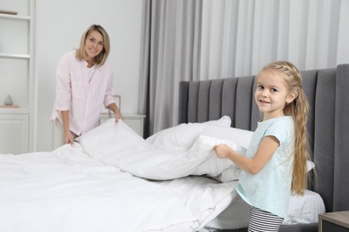 Photo of Little girl helping her mother making bed at home