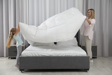 Photo of Little girl helping her mother making bed at home