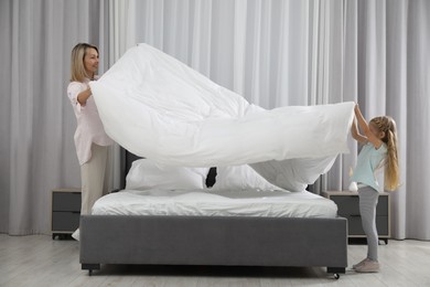 Photo of Little girl helping her mother making bed at home