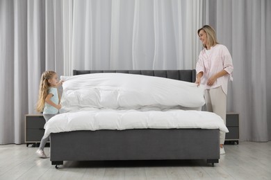 Photo of Little girl helping her mother making bed at home