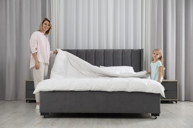 Photo of Little girl helping her mother making bed at home