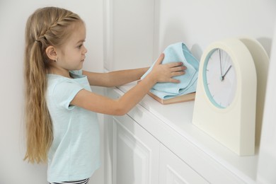 Photo of Little helper. Cute girl wiping dust at home