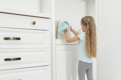 Photo of Little helper. Cute girl wiping dust from clock at home