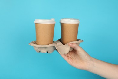 Photo of Woman holding holder with paper cups against light blue background, closeup. Mockup for design