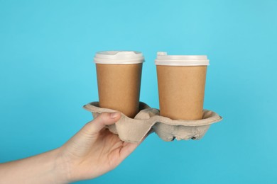 Photo of Woman holding holder with paper cups against light blue background, closeup. Mockup for design