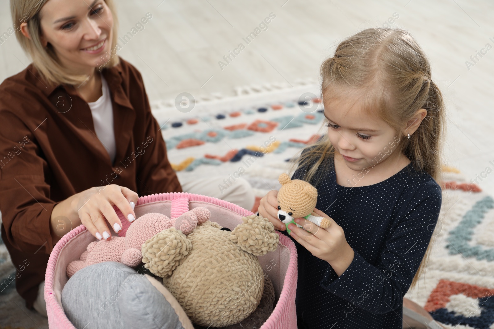 Photo of Little helper. Daughter and mother putting away toys together at home, closeup