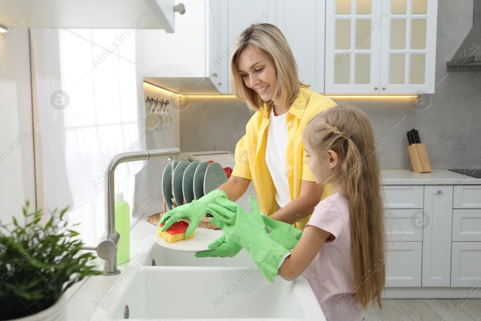 Photo of Little girl helping her mother washing dishes at home