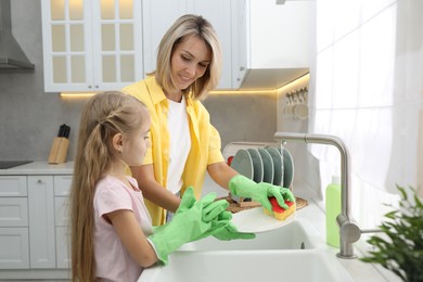 Little girl helping her mother washing dishes at home