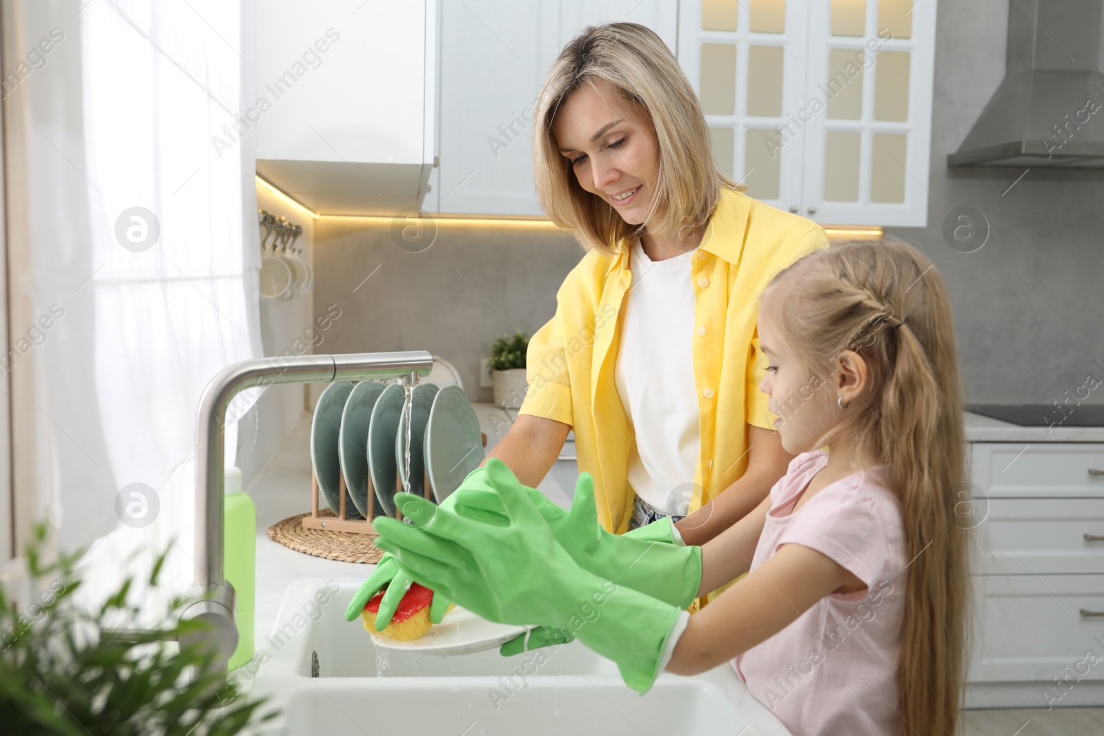 Photo of Little girl helping her mother washing dishes at home