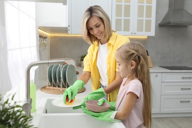 Photo of Little girl helping her mother washing dishes at home