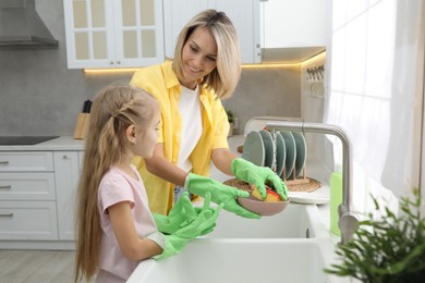 Photo of Little girl helping her mother washing dishes at home