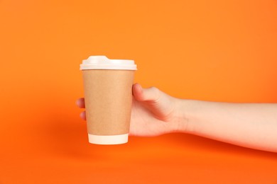 Photo of Woman holding paper cup on orange background, closeup. Mockup for design