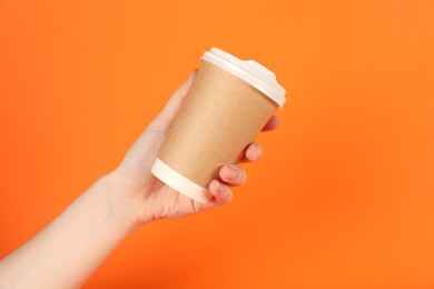 Photo of Woman holding paper cup on orange background, closeup. Mockup for design