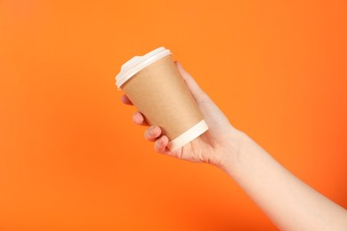 Photo of Woman holding paper cup on orange background, closeup. Mockup for design