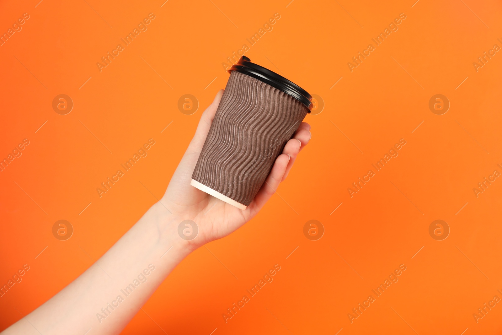 Photo of Woman holding paper cup on orange background, closeup. Mockup for design