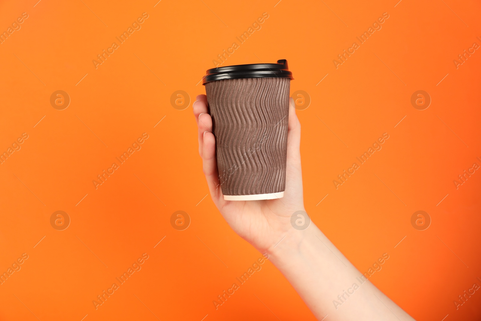 Photo of Woman holding paper cup on orange background, closeup. Mockup for design