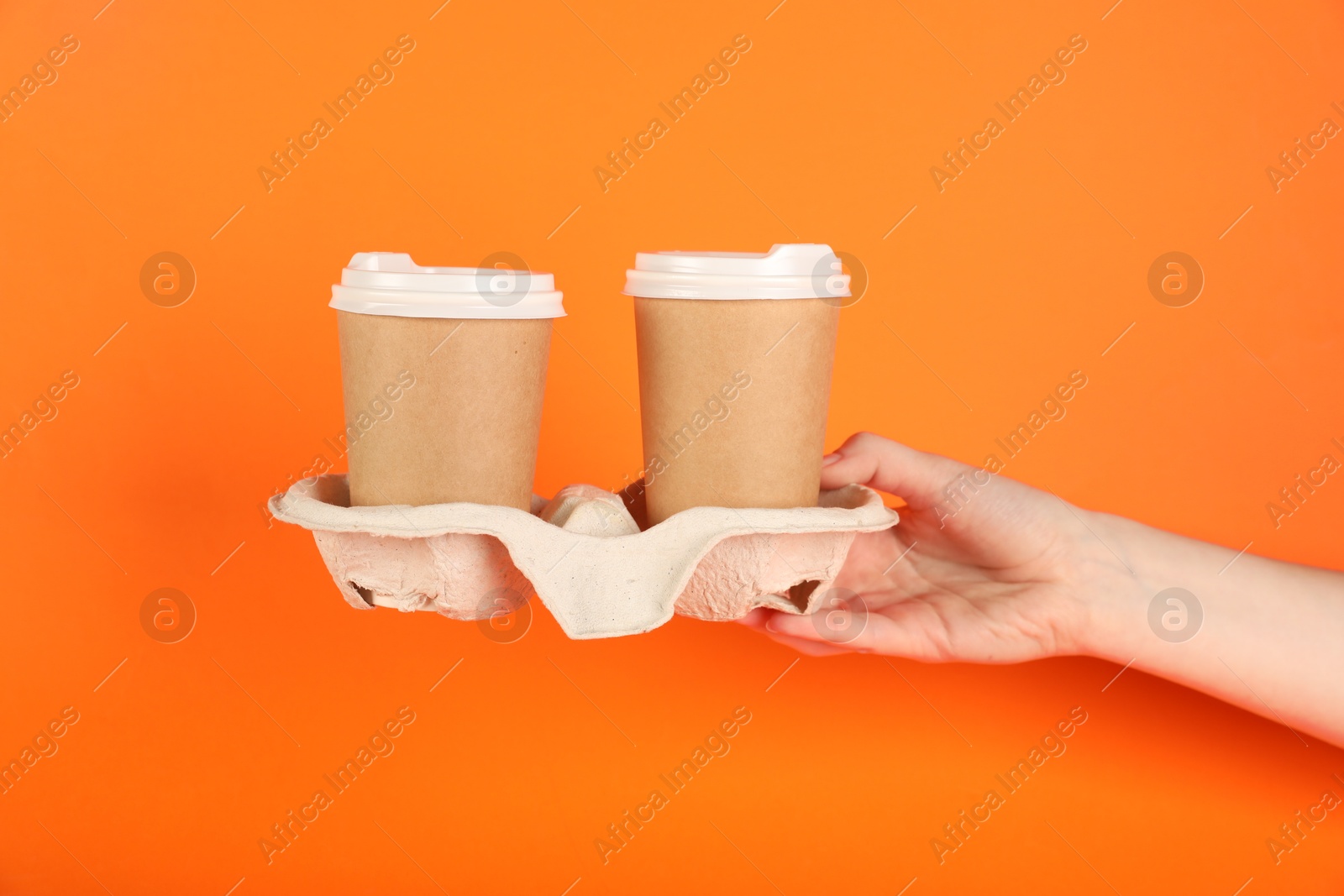 Photo of Woman holding holder with paper cups on orange background, closeup. Mockup for design