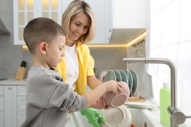 Photo of Little boy helping his mother washing dishes at home