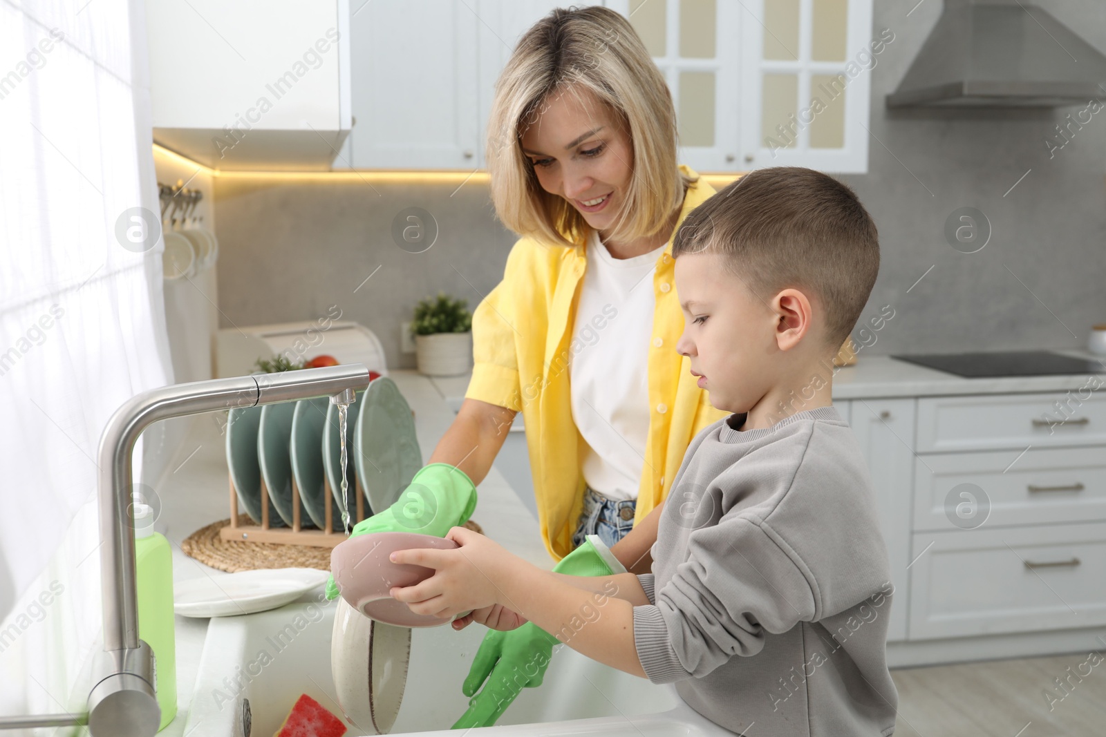 Photo of Little boy helping his mother washing dishes at home