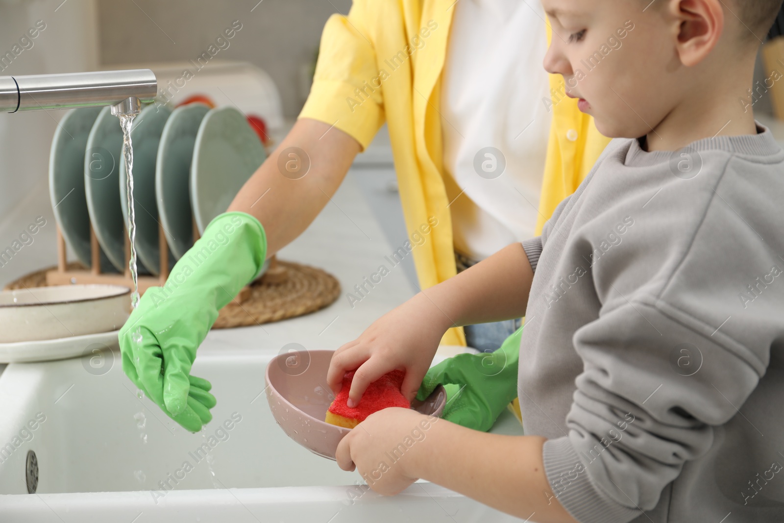 Photo of Little boy helping his mother washing dishes at home, closeup