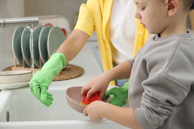 Photo of Little boy helping his mother washing dishes at home, closeup