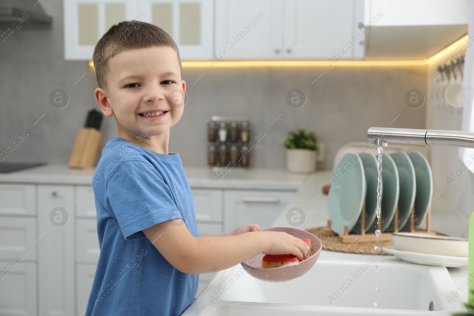 Photo of Little helper. Cute boy washing dishes at home