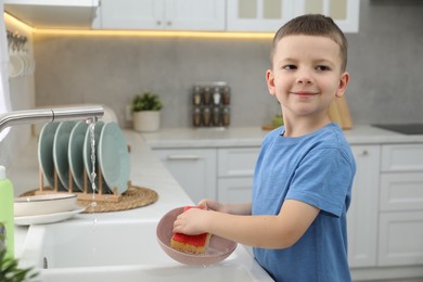 Photo of Little helper. Cute boy washing dishes at home