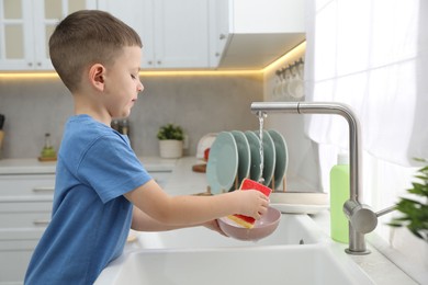 Photo of Little helper. Cute boy washing dishes at home