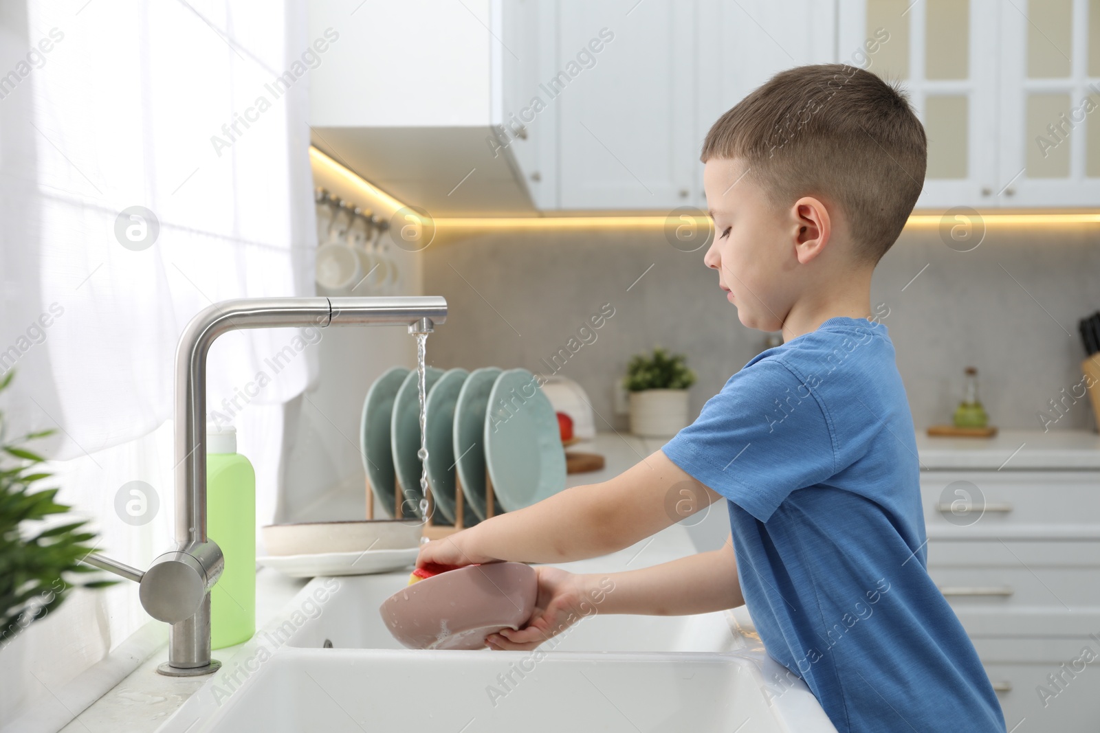 Photo of Little helper. Cute boy washing dishes at home