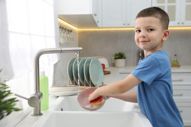 Photo of Little helper. Cute boy washing dishes at home